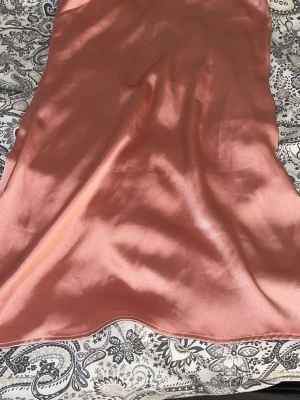 Rosa satin klänning med snörning - Säljer en kort, glansig rosa klänning i satin med tunna axelband och snygg snörning i ryggen. Perfekt för dig som vill ha en stilren look med lite extra detalj. Djur finns i hemmet, tvättas innan leverans.🌸