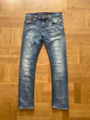 Nudie Jeans - Säljer ett par klassiska blå jeans från Nudie Jeans med snyggt slitna detaljer och raka ben. Jeansen har fem fickor, orange sömmar och en skinnpatch bak i midjan. Perfekta för dig som gillar en avslappnad och tidlös stil i väldigt bra skick!