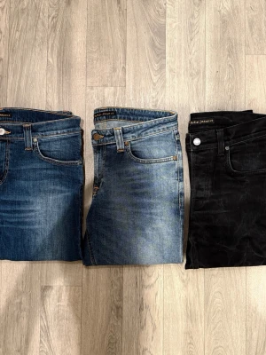 Tre par Nudie Jeans Herr Blå Svarta - Mycket fint skick utan defekter.  Jeans till vänster: Nudie Jeans Tight Long John W30/L34, Midja: 39,5cm, Ytterbenslängd: 106,5cm, Benöppning: 16cm  Jeans i mitten: Nudie Jeans Skinny Sam Org. Spring Blue W29/L34, Midja: 39,5cm, Ytterbenslängd: 107,5cm, Benöppning: 15cm  Jeans till höger: Nudie Jeans Grim Tim Dry Cold Black W30/L34, Midja: 37cm, Ytterbenslängd: 106,5cm, Benöppning: 16cm