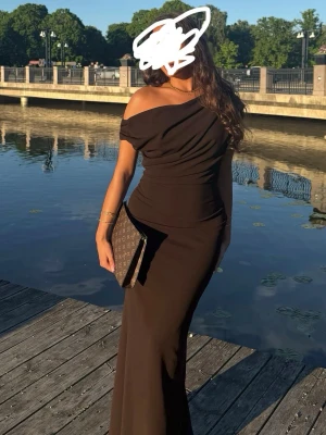 Brun one shoulder långklänning - Brun balklänning från bubbleroom, endast använd 1 gång i fåtal timmar, helt i nyskick! Säljer en elegant brun långklänning med draperad överdel och off shoulder-design. Klänningen har figurnära passform och slät kjol som faller snyggt längs kroppen. Perfekt för dig som vill ha en stilren och trendig look. 