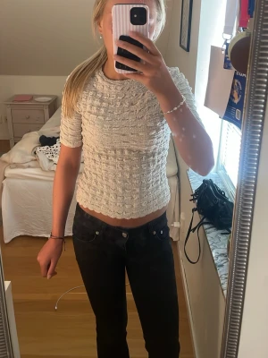 Vit ribbad topp från Lindex - Säljer en söt vit ribbad topp från Lindex i storlek XS. Toppen har korta ärmar, croppad passform och ett strukturerat tyg med vågig kant nertill. Perfekt att styla med jeans eller kjol för en trendig look.
