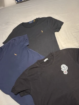 3-pack t-shirts från Moncler & Polo Ralph Lauren - Säljer tre snygga t-shirts: en svart Moncler med stor logga på bröstet, en mörkblå och en svart från Polo Ralph Lauren med den klassiska broderade loggan. Alla har rund hals och korta ärmar. Perfekta basplagg till garderoben.