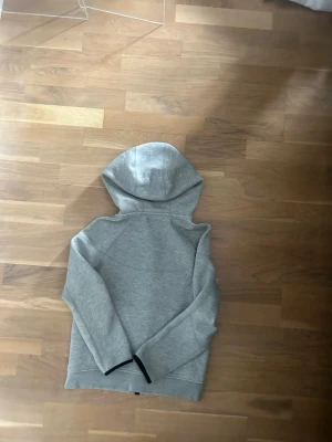 Grå hoodie från Nike med huva - Säljer en stilren grå hoodie från Nike med klassisk huva och långa ärmar. Hoodien har en enkel design utan tryck och är gjord i mjukt material som passar perfekt till chill dagar. Svart detalj vid ärmslut ger en snygg kontrast. Och är såklart äkta, hör av er vid frågor 👍