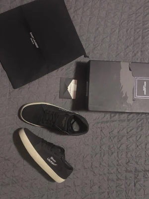 Svarta Saint Laurent court classic sneakers  - Säljer ett par otroligt stilrena Saint Laurent skor! Ett par fräscha svarta sommar skor med ett Saint Laurent tryck på sidan och en ”YSL Paris” logga på tungan. Perfekt för nån som söker ett par grisch och clean skor. Säljer dem med låda och dustbag🔥🙌 Skriv till mig så kan vi diskutera priset. 