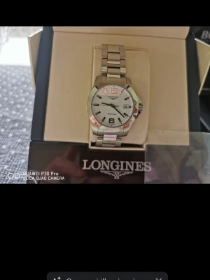 Longines silverfärgad klocka. - Stilren klocka från Longines med silverfärgat armband i metall och vit urtavla. Klockan har tydliga svarta siffror, datumvisning och klassisk design. Perfekt accessoar för dig som gillar tidlös och elegant stil. Kontakta mig privat