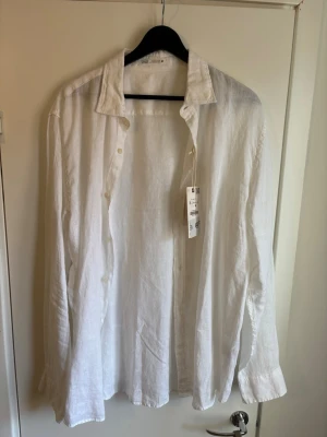 Vit linneskjorta från Zara XL - Snygg vit skjorta från Zara i luftig linnekvalitet. Klassisk krage, knäppning framtill och långa ärmar. Perfekt för en stilren och avslappnad look. Skjortan är enkel att matcha och passar till många olika outfits.