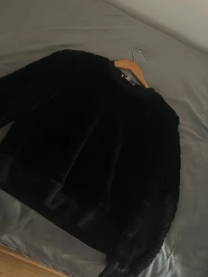 Svart fuskpälströja Crave Fame XS - Säljer en svart fuskpälströja från Crave Fame i storlek XS. Tröjan har en klassisk rak passform och är tillverkad i mjukt, fluffigt material som ger en lyxig känsla. Perfekt för att hålla värmen under kalla dagar och ger en snygg look.