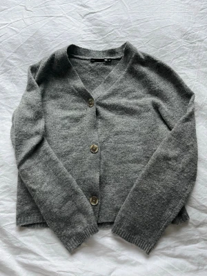 Grå kofta med knappar från Lager157 - Mysig grå kofta från Lager157 med tre knappar framtill och v-ringning. Långärmad modell i mjukt stickat material. Enkel och stilren design som passar till det mesta. Sparsamt använd! 