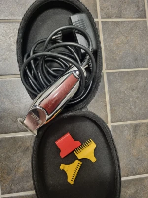 Wahl hårtrimmer med tillbehör - Elektrisk hårtrimmer från Wahl i silver och rött med svart sladd. Den är lite skadad i några tānder men inget som påverkar funktionen, eller om man vill laga den för den handige, nypris ca 1400.Medföljer tre plastkammar i rött och gult samt en praktisk svart förvaringsväska. Perfekt för att fixa frisyren hemma eller trimma skägget.