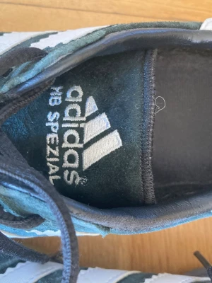 Adidas HB Spezial sneakers mörkgröna str. 40 - Adidas HB Spezial sneakers i mörkgrön mocka med klassiska vita ränder på sidorna och vit häl. Lågt skaft och svarta skosnören. Ikonisk retrostil med broderad logga på plösen. Perfekta för dig som gillar streetwear och sportig look. Storlek 40 (24,5 cm)