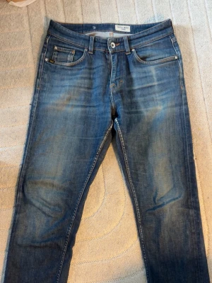 Tiger of Sweden Jeans 31/30 - Snygga blå jeans från Tiger of Sweden med lite slitningar/fade framtill. Jeansen har raka ben och orangea kontrastsömmar. Perfekta för en stilren och avslappnad look. Jeansen är i hyffsat skick och är riktigt snygga. Hör av er vid minsta fundering eller för fler bilder!