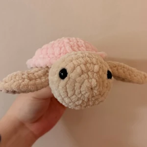 Sköldpadda med rosa skal - Supergullig mjukissköldpadda i beige plysch med ett fluffigt ljusrosa skal och stora svarta ögon. Perfekt som dekoration eller gosedjur. Tillverkad i mjukt tygmaterial och har en rund, söt form som är lätt att hålla i.