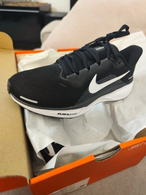 Nike Air Zoom svart/vit sneaker - Snygga Nike Air Zoom sneakers i svart mesh med vit sula och vit swoosh-logga på sidan. Skon har en sportig design med lågt skaft och bekväm dämpning. Perfekt för dig som gillar stilrena och funktionella sneakers. Denna sko är löpnings sko men funkar även som en vanlig sko, skorna är helt nya och oanvända!!