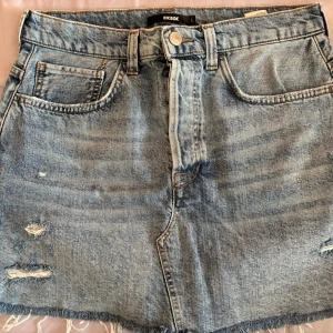  Jeanskjol från BikBok - Säljer en snygg blå jeanskjol från BikBok i storlek L.  Tillverkad i denim med knapp och dragkedja framtill. Perfekt för sommaren🌸