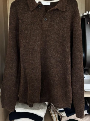 Brun stickad tröja från Selected Homme - Mysig brun stickad tröja från Selected Homme med krage och två knappar framtill. Tröjan har lång ärm och är tillverkad i ett fluffigt, mjukt material som känns riktigt skönt mot huden. Perfekt för kyliga dagar.