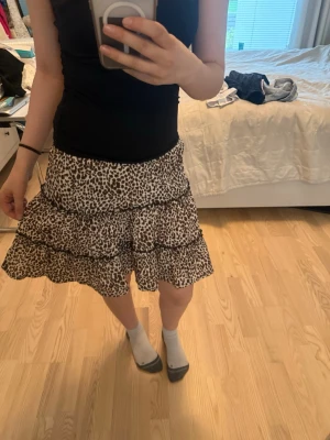 Leopardmönstrad volangkjol - Storlek 152! Snygg kort kjol med leopardmönster och flera volanger. Kjolen har resår i midjan och är i en lätt och luftig modell, perfekt för dig som gillar att sticka ut. Färgerna går i vitt, brunt och svart. Superfin att matcha med en enkel topp.