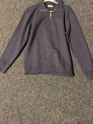 Mörkblå half-zip hoodie These Glory Days - Mörkblå hoodie från These Glory Days med halv dragkedja framtill och hög krage. Tillverkad i mjukt bomullsmaterial och har en stilren, minimalistisk design utan tryck eller mönster. Perfekt för en avslappnad och snygg look.