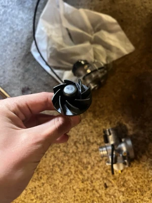 Svart turbinhjul till moped - Säljer ett svart turbinhjul med axel, troligen till moped eller mindre motorfordon. Hjulet är gjort i metall och har flera böjda blad för att skapa luftflöde. Perfekt för dig som gillar att meka med mopeder eller behöver reservdelar.