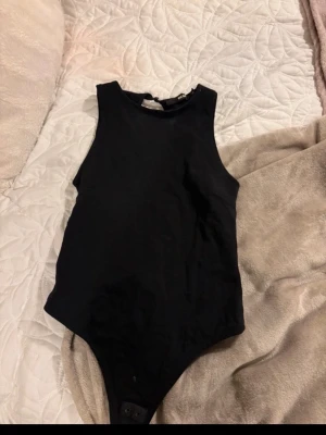 Svart ärmlös body - Säljer en enkel och stilren svart body med hög hals och ärmlös design. Bodyn har öppen rygg 