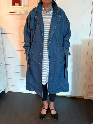Oversized denim trenchcoat Levi’s - Snygg oversized trenchcoat från Levi’s i blå denim med dubbelknäppning och bälte i midjan. Jackan har klassiska slag, fickor på sidorna och justerbara ärmslut. Perfekt för dig som gillar en avslappnad och trendig look. Helt ny med prislappen kvar.
