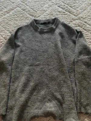 Grå stickad tröja från H&M - Mysig grå stickad tröja från H&M med rund halsringning och långa ärmar. Tröjan har en enkel och stilren design, perfekt att matcha med jeans eller kjol. Materialet känns mjukt och bekvämt mot huden.