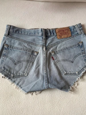 Levi's ljusblå jeansshorts 501 - Ljusblå jeansshorts från Levi's modell 501 med råa, fransiga kanter och klassiska fem fickor. 