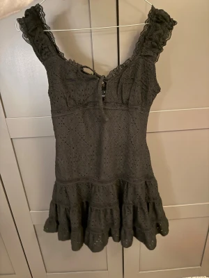 Svart spetsklänning med volang - Supersöt svart klänning med broderad spets, volangkant nertill och knytning vid bysten. Ärmlös modell med breda axelband och romantiska detaljer. Perfekt för dig som gillar en feminin och trendig stil. Den har tyvärr inte kommit till användning och har därför prislappen kvar. Den är liten i storleken! 