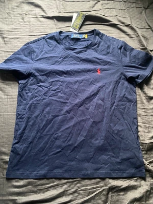 Ralph Lauren tröja - Snygg marinblå t-shirt från Polo Ralph Lauren med klassisk röd logga broderad på bröstet. Tillverkad i mjuk bomull och har en normal passform med korta ärmar. Perfekt basplagg för en clean och stilren look.