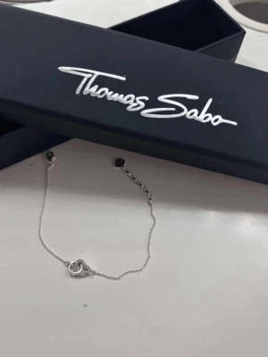 Silverarmband från Thomas Sabo - Snyggt och stilrent armband i silver från Thomas Sabo. Tunt kedjearmband med en liten cirkelformad detalj i mitten. Perfekt accessoar för att lyfta din outfit med en diskret touch av elegans. Levereras i originalask.