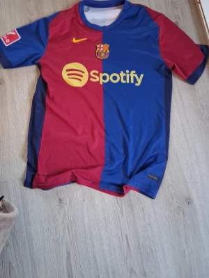 FC Barcelona matchtröja Lewandowski - Säljer en officiell FC Barcelona matchtröja från Nike med Lewandowski och nummer 9 på ryggen. Tröjan är röd och blå med gula detaljer, Spotify-logga på bröstet och UNHCR-logga bak. Tillverkad i lätt och ventilerande material, perfekt för fotboll eller träning.