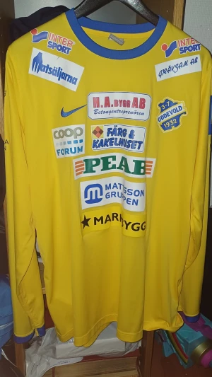 Ik Oddevold  - Gul långärmad fotbollströja från Nike med blå detaljer och flera sponsormärken. Tröjan har klubbmärke för IK Oddevold, nummer 10 på ryggen och tryckta loggor på både fram- och baksida. Storlek Xl, tröjan är äkta och är matchworn. Vissa sponsorer kan har lite slitage. Tröjan är från 2019 - 2020 säsongen.