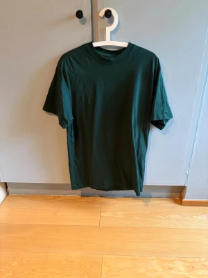 Mörkgrön basic t-shirt - En enkel mörkgrön t-shirt i klassisk modell från weekday med rund hals och korta ärmar. Storlek S men lite oversize så passar större.
