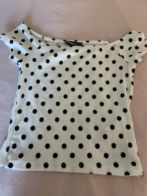Vit prickig topp från New yoker - Söt vit topp med svarta prickar från New yoker. Modellen är offshoulder med korta ärmar och har en figurnära passform. Den är ganska liten i storlek💓