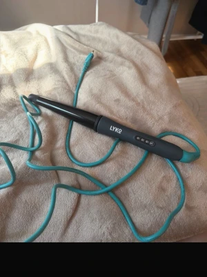 Svart konformad locktång från Lyko - Konformad locktång från Lyko i svart med turkos sladd. Perfekt för att skapa snygga lockar och vågor. Ergonomiskt handtag och digitala knappar för enkel användning. Sladden är lång och flexibel för smidig styling. använt max 3 gånger 