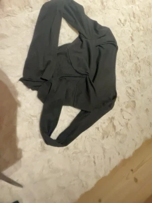 Svart långärmad croppad tröja - Säljer en svart långärmad croppad tröja med v-formad nederkant. Tröjan är figurnära och har en snygg, enkel design som passar perfekt till jeans eller kjol. Materialet känns mjukt och stretchigt, vilket gör den bekväm att bära.