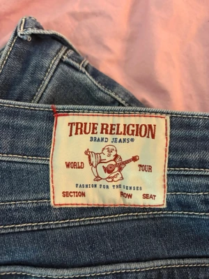 True Religion Joey Low Rise Flare Jeans - Säljer ett par blå True Religion jeans, modell Joey Low Rise Flare. Jeansen har låg midja och utsvängda ben, klassisk femficksdesign och tydliga kontrastsömmar. Perfekta för dig som gillar en retroinspirerad look med ikonisk passform.pris kan absolut diskuteras💗💗jeansen är nästan helt nya inga defekter är 173 cm💗💗