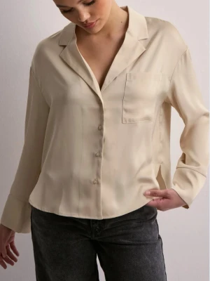 Beige satinblus med krage - Stilren beige blus i satin med klassisk krage och bröstficka. Knäppning framtill och långa ärmar ger en avslappnad men ändå chic look. Den är inte exakt likadan som på bilden.
