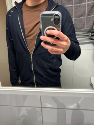 Zip sweatshirt Lindebergh - Säljer en mörkblå hoodie med dragkedja och huva. Tröjan har långa ärmar och en enkel, stilren design utan synliga loggor eller tryck. Perfekt för en avslappnad och bekväm stil.