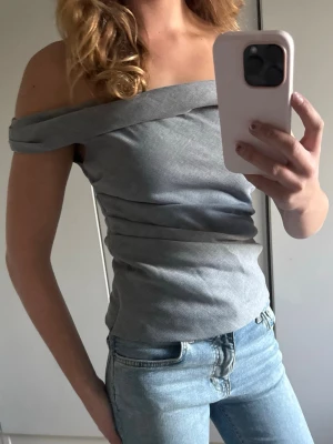 Grå offshoulder topp - Snygg grå offshoulder topp med åtsittande passform och bred kant upptill. Perfekt för dig som vill ha en stilren och trendig look. Toppens material känns mjukt och följsamt mot kroppen.