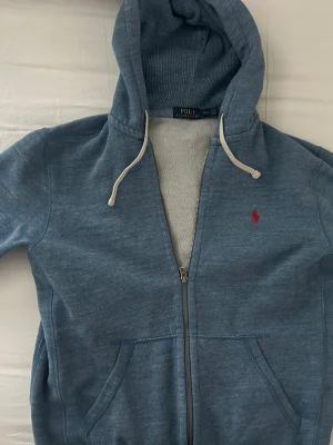  Polo Ralph Lauren zip hoodie  - Snygg blå zip-hoodie från Polo Ralph Lauren med klassisk röd logga broderad på bröstet. Hoodien har dragsko i huvan, två fickor framtill och är tillverkad i mjukt bomullsmaterial. Perfekt för en avslappnad och stilren look. Har knappt använd tröjan, typ 3 gånger. Pris kan diskuteras, o de är bara att skriva om du undrar något🙌🏻