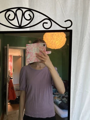 Ljuslila topp med puffärm - Säljer en ljuslila topp med puffiga kortärmar och rund halsringning. Toppen har en avslappnad passform och är gjord i 100% mjukt bomullsmaterial. Perfekt för dig som gillar en enkel men söt stil.