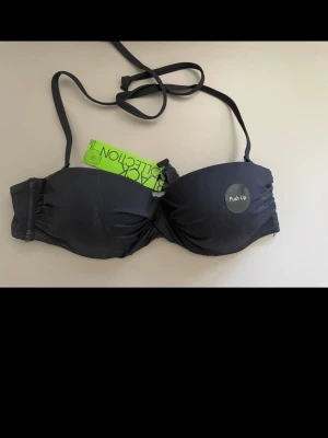 Svart push up-bikini bh Black Collection - Snygg svart push up-bikini bh från Black Collection med avtagbara axelband och vadderade kupor. Bh:n har en enkel knäppning fram och slät design som ger extra lyft. Perfekt för dig som vill ha en klassisk och stilren look. OBS! Kolla 2 sista  bilder. Ny med prislappen på men mindre skavanker. Och måste tvättas innan användning , finns spår efter provningar. Köpte den så . 