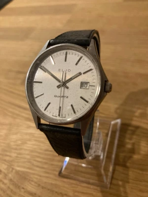 1980 Eljo Date Swiss Made 35mm Herrur - Säljer en stilren vintage dressklocka från schweiziska Eljo i gott skick enligt bilder. Finns tecken på användning som inte stör. Fungerar bra, läderarmband, datumvisare, mineralglas, Quartz urverk, boett i rostfritt stål, vattentät osv. Behöver bara nytt batteri. Modell: QA531.  Begagnat värde: < 1500 SEK Mitt pris: 489 SEK  Skickas snabbt och spårbart. Skriv vid frågor och se gärna mina andra annonser!