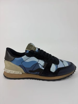 Valentino blå camo sneakers - Snygga sneakers från Valentino med blått camo-mönster, svarta detaljer och beige häl med nitar. Skorna har svarta skosnören, svart sula och ovandel i läder och mocka. Perfekta för dig som vill sticka ut med en unik och trendig stil.