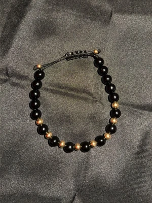 Svart och guldigt pärlarmband - Snyggt armband i 18k guld och svarta onyx pärlor på svart justerbart snöre. Perfekt accessoar för dig som gillar stilrena detaljer och vill addera lite klass till din look.