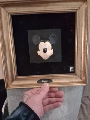 Inramad Mickey Mouse-dekoration - Säljer en unik inramad dekoration med Mickey Mouse-huvud i keramik från jie keramik. Svart bakgrund och guldfärgad ram ger en cool kontrast. Perfekt för dig som gillar Disney och vill ha något annorlunda på väggen.
