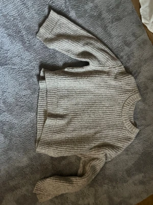 Beige stickad tröja Gina Tricot - Mysig beige stickad tröja från Gina Tricot med grov ribbstickning. Tröjan har rund halsringning, långa ärmar och breda muddar vid ärmslut och nederkant. Perfekt för lager på lager och enkel att matcha med jeans eller kjol.