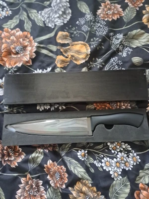 Ny Kockkniv i originalförpackning– Oanvänd! - Säljer en rejäl och stilren kockkniv som är helt **oanvänd** och ligger kvar i sin **originalförpackning**. Kniven har ett svart, ergonomiskt handtag som ger ett stadigt och säkert grepp. Detta är en utmärkt allroundkniv för köket eller en perfekt present till någon som precis flyttat hemifrån. Den eleganta svarta lådan gör att den ser mycket professionell ut vid överlämning. Skick: Oanvänt (aldrig använd). Tillbehör: Levereras i svart originalask med skydd för knivspetsen.