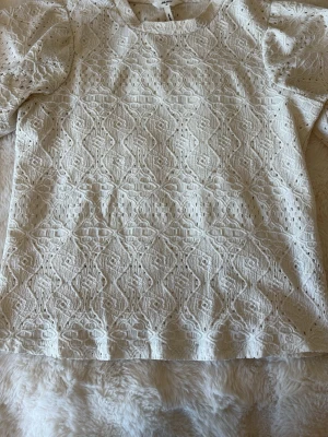 Vit spetsblus med kort ärm  - Superfin vit blus från object  med korta ärmar och vackert spetsmönster över hela toppen. Blusen har rund halsringning och är tillverkad i ett lätt och luftigt material som känns fräscht och somrigt.