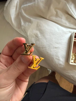 Louis Vuitton LV örhängen i guld - Säljer ett par ikoniska Louis Vuitton örhängen i form av LV-loggan. De är i guldfärgad metall och har en stilren, modern design som verkligen sticker ut. Perfekta för dig som gillar lyxiga accessoarer och vill ha något som syns.